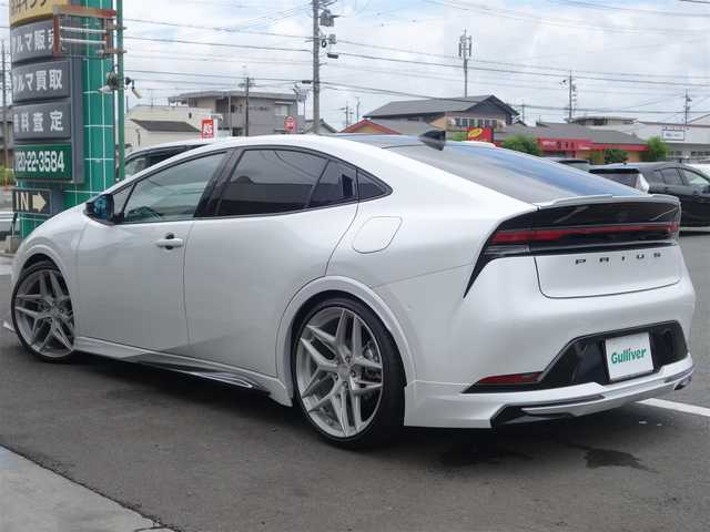 トヨタ プリウス Z 静岡県 2023(令5)年 0.7万km プラチナホワイトパールマイカ ワンオーナー・禁煙車/＜外装＞/モデリスタNEO ADVANCE STYLEエアロ/　フロントスポイラー/　サイドスカート/サイドガーニッシュ/　リヤスタイリングキット/　GRテールゲートスポイラー同色塗装/　フロント・リヤアーチ周り同色塗装/TEIN FREX車高調整キット/　アライメント調整済み/WORK グノーシス20インチAW/　タイヤ前後アゼニス225/35ZR20/パノラマルーフ・パワーバックドア/＜内装＞マチュアレッド色/12.3型ディスプレイオーディオプラス/コネクティッドナビ　フルセグ（TVキット）/パノラミックビューモニター/ビルトインETC2.0/純正デジタルインナーミラー/トヨタセーフティーセンス/　トヨタチームメイト/　メーカーオプション/　ドライブレコーダー前後方/　ブラインドスポットモニター/　安心降車アシスト+後方車両接近/　周辺車両接近時サポート/　後方車両への接近警報/　セカンダリーコリジョンブレーキ/ワイヤレス充電器/純正レクサスNX用シフトノブ/前席シートヒーター・ベンチレーション/アクセサリーコンセント/　AC100V 1500W/各種社外ピアノブラックパネル/純正フロアマット/　