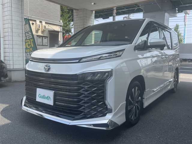 トヨタ ヴォクシー ハイブリッド S－Z 愛知県 2023(令5)年 1万km ホワイトパールクリスタルシャイン モデリスタエアロ/・フロント／サイド／リアアンダー/快適利便パッケージHifh/・ハンズフリー両側パワースライドドア/・ハンズフリーパワーバックドア/・2列目シートヒーター/・2列目オットマン/・ステアリングヒーター/・ナノイーX/ドライビングサポートパッケージ/・デジタルインナーミラー/・ヘッドアップディスプレイ/純正10.5型ディスプレイオーディオプラス/・車載メモリーナビ／DVD／Bluetooth／地デジTV/・Apple Car Play／Android Auto/・USB／HDMI/・ビルトインETC2.0/純正14型有機ELフリップダウンモニター/LEDヘッドライト＆クリアランスランプ/合皮＆ファブリックコンビシート/前席2列目シートヒーター/2列目充電用USBタイプC端子/ラゲッジルームアクセサリーコンセント/純正17インチAW/スマートキー