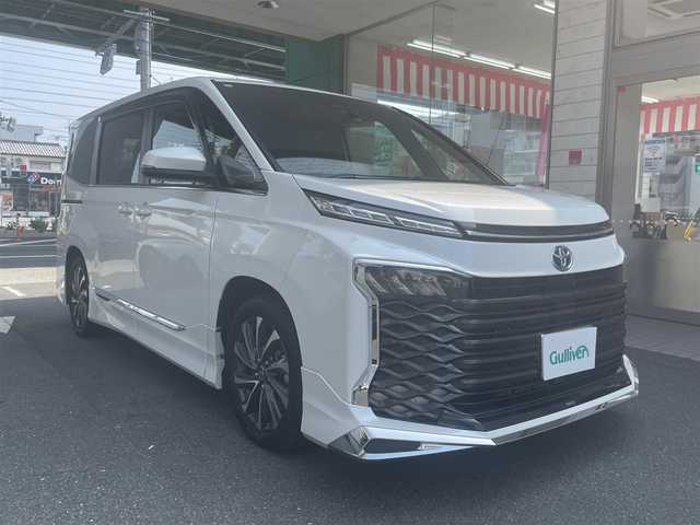トヨタ ヴォクシー ハイブリッド S－Z 愛知県 2023(令5)年 1万km ホワイトパールクリスタルシャイン モデリスタエアロ/・フロント／サイド／リアアンダー/快適利便パッケージHifh/・ハンズフリー両側パワースライドドア/・ハンズフリーパワーバックドア/・2列目シートヒーター/・2列目オットマン/・ステアリングヒーター/・ナノイーX/ドライビングサポートパッケージ/・デジタルインナーミラー/・ヘッドアップディスプレイ/純正10.5型ディスプレイオーディオプラス/・車載メモリーナビ／DVD／Bluetooth／地デジTV/・Apple Car Play／Android Auto/・USB／HDMI/・ビルトインETC2.0/純正14型有機ELフリップダウンモニター/LEDヘッドライト＆クリアランスランプ/合皮＆ファブリックコンビシート/前席2列目シートヒーター/2列目充電用USBタイプC端子/ラゲッジルームアクセサリーコンセント/純正17インチAW/スマートキー