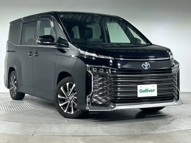 トヨタ ヴォクシー ハイブリッド S－Z 神奈川県 2024(令6)年 0.4万km アティチュードブラックマイカ 純正10.5型ディスプレイオーディオ/AM FM フルセグ Bluetooth CD DVD HDMI/バックカメラ/純正14型有機ELフリップダウンモニター/両側パワースライドドア/快適利便パッケージHigh/パワーバックドア/ステアリングヒーター/シートヒーター【1列目、2列目】/オットマン/角度調整付アームレスト/レーダークルーズコントロール/セーフティセンス/プリクラッシュセーフティ/レーントレーシングアシスト/レーンディパーチャーアラート/ロードサインアシスト/ドライバー異常時対応システム/プロアクティブドライビングアシスト/発進遅れ告知機能/フロントクロストラフィックアラート/レーンチェンジアシスト/パーキングサポートブレーキ/ブラインドスポットモニター/アドバンスドライブ/クリアランスソナー/ステアリングリモコン/ハーフレザーシート/ビルトインETC2.0/オートホールド/LEDヘッドライト/オートライト/オートマチックハイビーム/スマートキー/スペアキー/純正17インチアルミホイル