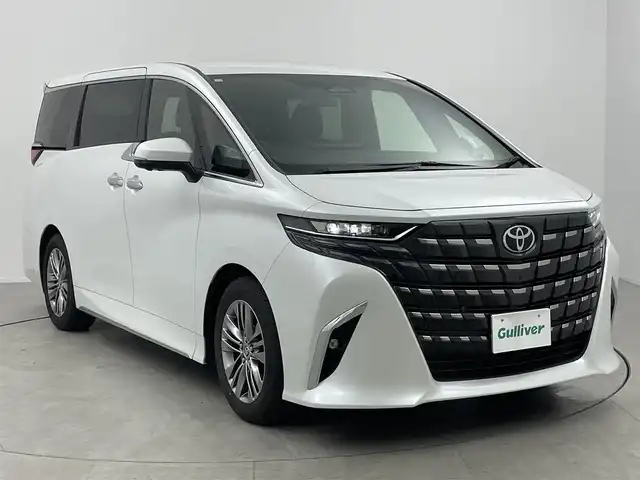 トヨタ アルファードハイブリット Z 愛知県 2024(令6)年 1.7万km プラチナホワイトパールマイカ 左右独立ムーンルーフ/13.2型有機EL後席ディスプレイ/14インチHDディスプレイオーディオ/(フルセグTV/BT/AM/FM)/合皮シート/前席＋二席目シートヒーター/前席＋二席目シートベンチレーション/全自動サンシェード/前後ドライブレコーダー/3眼LEDヘッドライト/ユニバーサルステップ/デジタルインナーミラー/トヨタセーフティセンス/・レーントレーシングアシスト/・プリクラッシュセーフティ/・ヘッドアップディスプレイ/・オートマチックハイビーム/・ブラインドスポットモニター/・クリアランスソナー/・パーキングサポートブレーキ/・アダクティブクルーズコントロール/ETC2.0/電動リアゲート/両側パワースライドドア/純正18インチAW/AC100V充電ソケット