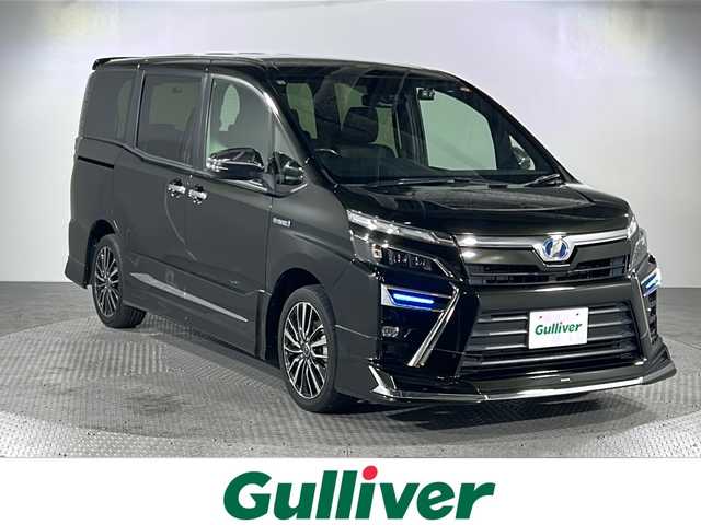 トヨタ ヴォクシー ハイブリッド ZS 煌 沖縄県 2018(平30)年 5.6万km イナズマスパーキングブラックガラスフレーク 禁煙車/県外仕入/7人乗り/純正10インチナビ/（フルセグTV/bluetooth/DVD/CD）/12.1インチフリップダウンモニター/前後ドライブレコーダー/モデリスタエアロ/フロントスポイラー/スタイリッシュモール/リアスカート/シグネチャーイルミブレード/トヨタセーフティセンス/プリクラッシュセーフティ/レーンディパーチャーアラート/オートマチックハイビーム/両側パワースライドドア/前席シートヒーター/ビルトインETC/純正フロアマット