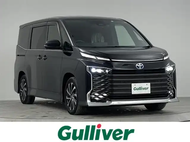 トヨタ ヴォクシー ハイブリッド S－Z 熊本県 2023(令5)年 2.9万km グリッターブラックガラスフレーク 純正10.5インチナビ/CD/DVD/フルセグTV/Bluetooth/純正14インチフリップダウンモニター/両側パワースライドドア/トヨタセーフティセンス/プリクラッシュセーフティ/レーンディパーチャーアラート/クリアランスソナー/パーキングサポートブレーキ/ロードサインアシスト/プロアクティブドライビングアシスト/快適利便パッケージ/ユニバーサルステップ/ハーフレザーシート/シートヒーター/オットマン/１００V充電/追従付きクルーズコントロール/オートハイビーム/前後ドライブレコーダー/ビルトインETC2.0/フロアマット/純正ドアバイザー/純正17インチアルミホイール