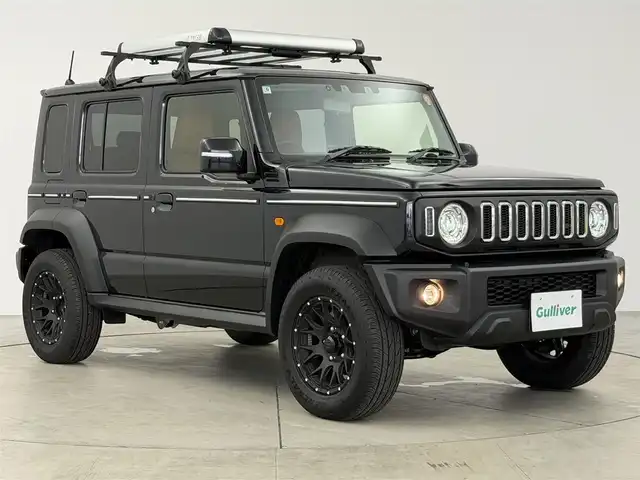 スズキ ジムニー ノマド FC 愛知県 2025(令7)年 0.1万km ブルーイッシュブラックパール3 10インチディスプレイオーディオ/ヒッチメンバー/ルーフキャリア/茶レザーシートカバー/背面タイヤ/ETC/４ＷＤ/デュアルブレーキサポート/レーダークルーズコントロール/シートヒーター（D+N)/ミラーヒーター/パーキングソナー/オートライト/社外16インチＡＷ/革巻きステアリング/ダウンヒルアシストコントロール/LEDヘッドライト/スマートキー/プッシュスタート/横滑り防止装置