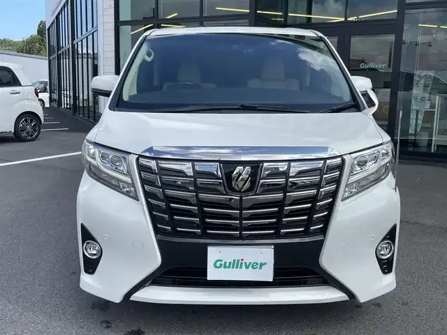 トヨタ アルファードハイブリット G Fパッケージ 愛媛県 2015(平27)年 9.8万km ラグジュアリーホワイトパールクリスタルシャインガラスフレーク 1オーナー/ツインサンルーフ/ALPINE専用10型ナビ【EX10】/　CD/DVD/Bluetooth/HDMI/フルセグTV/ガイド付きバックカメラ/ALPINE12.8型フリップダウンモニター/両側パワースライドドア/衝突被害軽減ブレーキ/クルーズコントロール/ステアリングヒーター/ベージュレザーシート/前席パワーシート(D席メモリー付)/前席シートヒーター/N席2列目オットマン/AC100Vアクセサリー/オートマチックハイビーム/オートライト/LEDヘッドライト/パワーバックドア/ビルトインETC/前後ドライブレコーダー/プッシュスタート/スペアキー×1/取説書