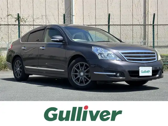 日産 ティアナ 250XL 東京都 2012(平24)年 9.9万km ディープアメジストグレー VDC/TCS/メッキ加飾横３本バーフロントグリル/開口部無塗装１本桟フロントバンパー/ボディ同色電動格納ミラー/ウィンカーミラー/リア標準バンパー/木目調加飾シルキーエクリュインパネ/ファインビジョンメーター（自発光式アナログメーター）/シルキーエクリュ革巻きステアリングホイール/SRSエアバック （運転席/助手席/サイド）/左右独立温度調整オートエアコン/後席エアコン吹出口/シルキーエクリュシート/パワーシート（運転席/助手席）パワーオットマン （助手席）/シート別体上下調整式ヘッドレスト（後席左右中央）/木目調カップホルダー付きアームレスト（後席中央）/インテリジェントキー/イモビライザー/プッシュエンジンスターター/７インチ液晶モニター/スーパーサウンドシステム１（６CD/６スピーカー）/バックモニター