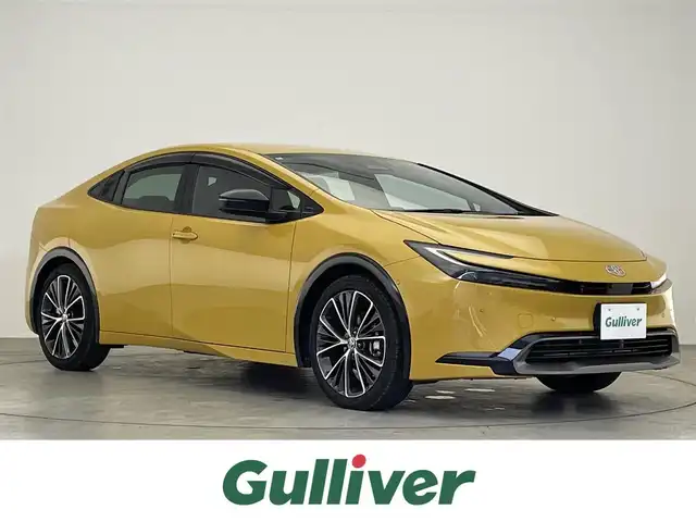 トヨタ プリウス Z 滋賀県 2024(令6)年 2万km ゴールド 禁煙車/純正ディスプレイオーディオ/（Miracast/Bluetooth/USB/フルセグTV）/パノラミックビューモニター/ビルトインETC/デジタルインナーミラー/プリクラッシュセーフティー/レーンディパーチャーアラート/ブラインドスポットモニター/プロアクティブドライビングアシスト/クリアランスソナー/リアクロストラフィックアラート/後方車両接近告知/リヤカメラディテクション/パーキングサポートブレーキ/安心降車アシスト/ロードサインアシスト/革巻きステアリング/レーダークルーズコントロール/ステアリングヒーター/ステアリングリモコン/パワーバックドア/レザーシート/D席シートメモリー/D席パワーシート/前席シートヒーター/前席ベンチレーション/LEDヘッドライト/フォグランプ/オートヘッドライト/オートマチックハイビーム/ヘッドライトレベライザー/電動パーキングブレーキ/オートホールドブレーキ/USB充電/AC100V/置くだけ充電/純正アルミホイール/社外フロアマット