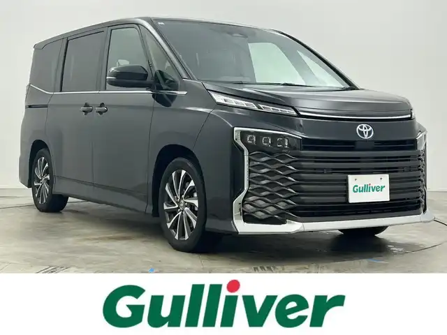 トヨタ ヴォクシー ハイブリッド S－Z 岡山県 2024(令6)年 1.9万km グリッターブラックガラスフレーク 快適利便パッケージ/ハーフレザーシート/純正10.5インチディスプレイオーディオ/　「ナビ/フルセグ/Bluetooth/DVD/ Carplay」/ブラインドスポットモニター/バックカメラ/ユニバーサルステップ（左回りのみ）/追従型クルーズコントロール/オートハイビーム/LEDヘッドライト/ビルトインETC2.0/両側パワースライドドア/シートヒーター(1列目/2列目)/衝突軽減ブレーキシステム/車線逸脱防止システム/横滑り防止装置/純正17インチアルミホイール/コーナーセンサー（前後）/純正フロアマット/ステアリングスイッチ/プッシュスタート/スマートキー×1