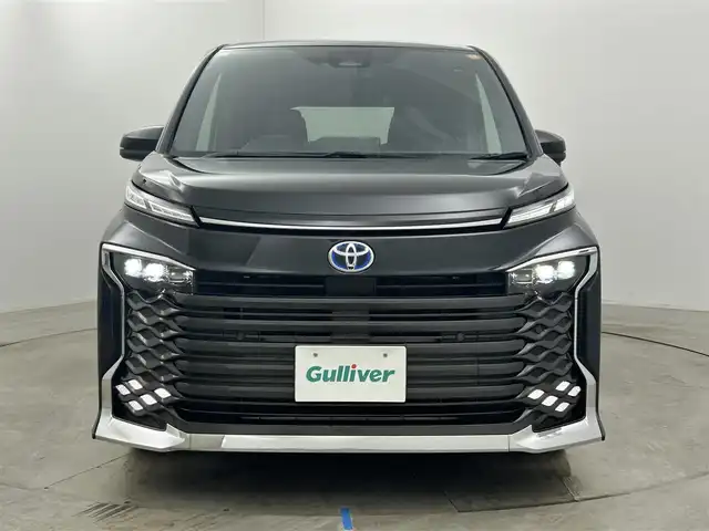 トヨタ ヴォクシー ハイブリッド S－Z 岡山県 2024(令6)年 1.9万km グリッターブラックガラスフレーク 快適利便パッケージ/ハーフレザーシート/純正10.5インチディスプレイオーディオ/　「ナビ/フルセグ/Bluetooth/DVD/ Carplay」/ブラインドスポットモニター/バックカメラ/ユニバーサルステップ（左回りのみ）/追従型クルーズコントロール/オートハイビーム/LEDヘッドライト/ビルトインETC2.0/両側パワースライドドア/シートヒーター(1列目/2列目)/衝突軽減ブレーキシステム/車線逸脱防止システム/横滑り防止装置/純正17インチアルミホイール/コーナーセンサー（前後）/純正フロアマット/ステアリングスイッチ/プッシュスタート/スマートキー×1