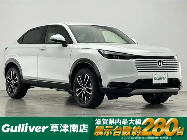 ホンダ ヴェゼル ハイブリッド e:HEV Z 滋賀県 2025(令7)年 0.1千km プラチナホワイトパール 純正9インチナビ/【Bluetooth/USB/Apple CarPlay/Android Auto/フルセグTV】/ハーフレザーシート/バックカメラ/ホンダセンシング/・衝突軽減ブレーキ/・先行車発進お知らせ機能/・歩行者事故低減ステアリング/・路外逸脱抑制機能/・標識認識機能/・渋滞追従機能付アダプティブクルーズコントロール/・車線維持支援システム（LKAS）/・トラフィックジャムアシスト（渋滞運転支援機能）/・ブラインドスポットインフォメーション/・誤発進抑制機能/・後方誤発進抑制機能/・近距離衝突軽減ブレーキ/・急アクセル抑制機能/・パーキングセンサーシステム/・後退出庫サポート/・オートハイビーム/・アダプティブドライビングビーム/LEDヘッドライト/クリアランスソナー/ヒルディセントコントロール/D/Nシートヒーター/ワイヤレス充電/ステアリングヒーター/ビルトインETC2.0/電動パーキングブレーキ/オートブレーキホールド/パワーバックドア/パドルシフト/プッシュスタート/スマートキー/ステアリングリモコン