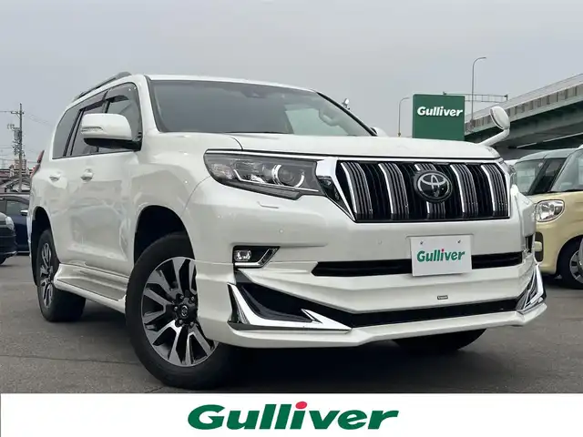トヨタ ランドクルーザー プラド TX Lパッケージ 愛知県 2023(令5)年 5.1万km ホワイトパールクリスタルシャイン 4WD/純正9型ナビ(BT/CD/DVD)/フルセグTV/バックカメラ/ビルトインETC/レーダークルーズコントロール/クリアランスソナー/セーフティセンス/・プリクラッシュセーフティ/・レーンディパーチャーアラート/・オートマチックハイビーム/・ロードサインアシスト/LEDヘッドランプ/木目調/革巻きコンビステアリング/ニュートラルベージュ革シート/前席パワーシート/快適温熱シート/3列目電動格納シート/純正19インチアルミホイール/スマートエントリー/スタートシステム/モデリスタエアロ