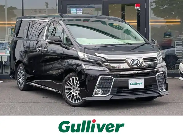 トヨタ ヴェルファイア Z Gエディション 福井県 2015(平27)年 8.9万km バーニングブラッククリスタルシャインガラスフレーク 純正18インチAW/ビルトインETC/レーダークルーズコントロール/衝突被害軽減システム/アイドリングストップ/１００V充電/後席用フリップダウンモニター/前席パワーシート/ステアリングヒーター/オットマン/電動リアゲート/両側パワースライドドア/前方ドライブレコーダー/前後コーナーセンサー/純正10インチメモリナビ（CD/DVD/BT/USB）/横滑り防止装置/盗難防止装置/LEDヘッドライト/スタッドレスタイヤ積込/社外シートカバー/オートホールド