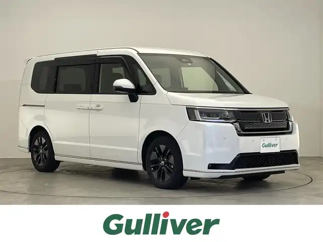 ホンダ ステップワゴン スパーダ eHEV 滋賀県 2022(令4)年 3.4万km プラチナホワイトパール 禁煙車/純正9型ナビ/（CD/DVD/Bluetooth/フルセグTV)/バックカメラ/ETC/前後ドラレコ/両側パワースライドドア/純正10.1型フリップダウンモニター/パワーバックドア/ハーフレザーシート/1列目シートヒーター/2列目オットマン/LEDヘッドライト/オートライト/ホンダセンシング/　・オートハイビーム/　・アダプティブドライビングビーム/　・渋滞追従機能付アダプティブクルーズコントロール/　・衝突被害軽減ブレーキ（CMBS)/　・近距離衝突軽減ブレーキ/　・車線維持支援システム（LKAS)/　・路外逸脱抑制機能/　・パーキングセンサーシステム/　・誤発進抑制機能/　・後方誤発進抑制機能/　・先行車発進お知らせ機能/　・標識認識機能/　・歩行者事故低減ステアリング/　・トラフィックジャムアシスト/　・ブラインドスポットインフォメーション/パドルシフト/電動パーキングブレーキ/オートブレーキホールド/プッシュスタート/スマートキー×２