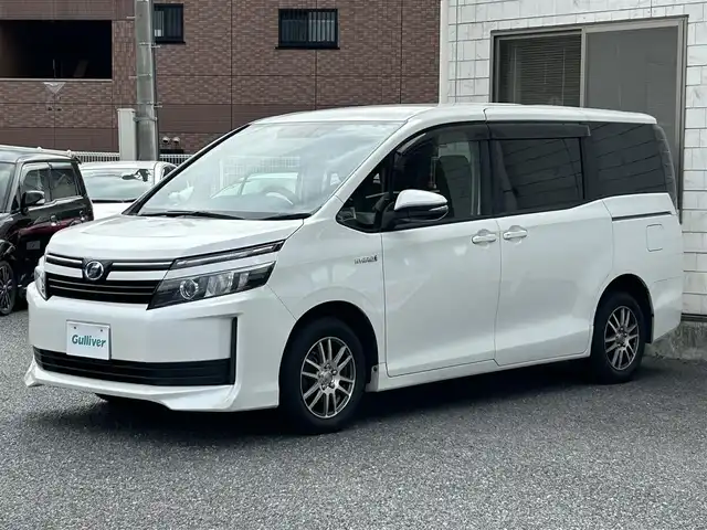 トヨタ ヴォクシー ハイブリッド X 福岡県 2015(平27)年 11.7万km ホワイトパールクリスタルシャイン 後部座席11インチフリップダウンモニター【V11T-R62C】/純正9インチメモリナビ【NSZT-Y64T】/　（AM/FM/CD/DVD/Bluetooth/フルセグTV）/バックカメラ/横滑り防止装置/オートライト/車両接近警報装置/両側パワースライドドア/社外15インチアルミホイール(サーキュラー)/ビルトインETC/コムテック製前後ドライブレコーダー【DC-DR652】/3列シート/社外フロアマット(YMT)/後部座敷サンシェード/電格ウインカーミラー/ドアバイザー/ステアリングスイッチ/電源ソケット×1/ISOFIX/スペアキー×1/保証書/取扱説明書/ナビ取扱説明書