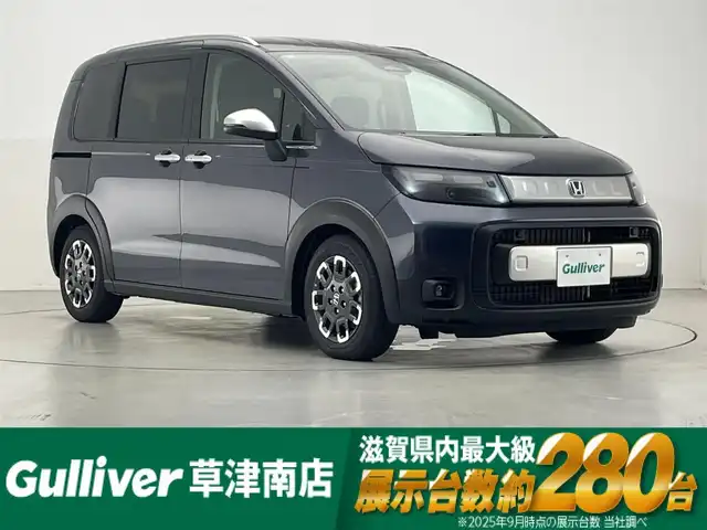 ホンダ フリード ハイブリット e:HEV クロスター 滋賀県 2025(令7)年 0.1千km メテオロイドグレーメタリック 登録済未使用車/純正9インチナビ/【Bluetooth/USB/フルセグTV/Apple CarPlay/Android Auto】/ハーフレザーシート/両側パワースライドドア/バックカメラ/ホンダセンシング/・衝突軽減ブレーキ/・先行車発進お知らせ機能/・歩行者事故低減ステアリング/・路外逸脱抑制機能/・標識認識機能/・渋滞追従機能付アダプティブクルーズコントロール/・車線維持支援システム（LKAS）/・トラフィックジャムアシスト（渋滞運転支援機能）/・ブラインドスポットインフォメーション/・誤発進抑制機能/・後方誤発進抑制機能/・近距離衝突軽減ブレーキ/・急アクセル抑制機能/・パーキングセンサーシステム/・オートハイビーム/・アダプティブドライビングビーム/LEDヘッドライト/D/Nシートヒーター/電動パーキングブレーキ/オートブレーキホールド/プッシュスタート/スマートキー/ステアリングリモコン