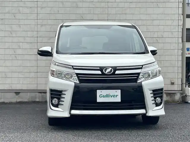 トヨタ ヴォクシー ZS 煌 大分県 2015(平27)年 9.1万km ホワイトパールクリスタルシャイン ・社外メモリーナビ（MDV-Z701W）/　CD/DVD/BT/フルセグ/・ETC/・両側パワースライドドア/・社外フリップダウンモニター/・革巻きステアリング/・スマートキー/・エンジンプッシュスタート/・ウインカーミラー/・ステアリングスイッチ/・フロアマット/・ドアバイザー/・プライバシーガラス/・アイドリングストップ/・横滑り防止システム/・後部座席サンシェード/・純正16インチアルミホイール/・LEDヘッドライト/・純正フォグランプ/・保証書/・取扱説明書