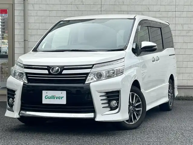 トヨタ ヴォクシー ZS 煌 大分県 2015(平27)年 9.1万km ホワイトパールクリスタルシャイン ・社外メモリーナビ（MDV-Z701W）/　CD/DVD/BT/フルセグ/・ETC/・両側パワースライドドア/・社外フリップダウンモニター/・革巻きステアリング/・スマートキー/・エンジンプッシュスタート/・ウインカーミラー/・ステアリングスイッチ/・フロアマット/・ドアバイザー/・プライバシーガラス/・アイドリングストップ/・横滑り防止システム/・後部座席サンシェード/・純正16インチアルミホイール/・LEDヘッドライト/・純正フォグランプ/・保証書/・取扱説明書
