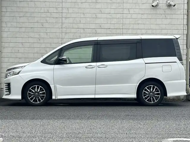 トヨタ ヴォクシー ZS 煌 大分県 2015(平27)年 9.1万km ホワイトパールクリスタルシャイン ・社外メモリーナビ（MDV-Z701W）/　CD/DVD/BT/フルセグ/・ETC/・両側パワースライドドア/・社外フリップダウンモニター/・革巻きステアリング/・スマートキー/・エンジンプッシュスタート/・ウインカーミラー/・ステアリングスイッチ/・フロアマット/・ドアバイザー/・プライバシーガラス/・アイドリングストップ/・横滑り防止システム/・後部座席サンシェード/・純正16インチアルミホイール/・LEDヘッドライト/・純正フォグランプ/・保証書/・取扱説明書