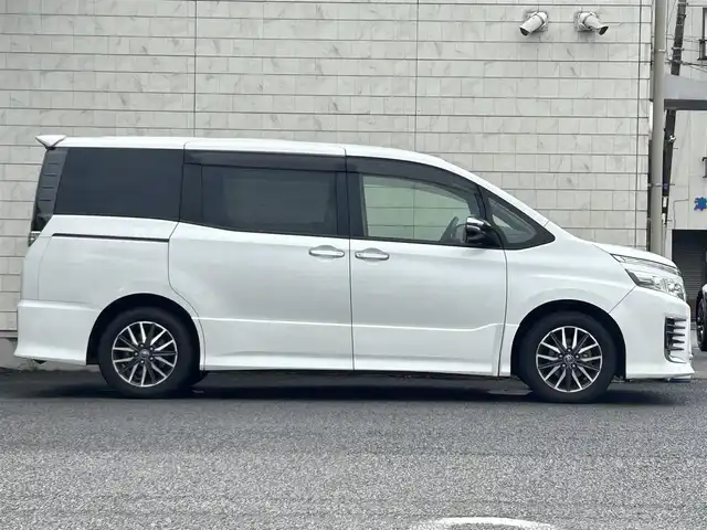 トヨタ ヴォクシー ZS 煌 大分県 2015(平27)年 9.1万km ホワイトパールクリスタルシャイン ・社外メモリーナビ（MDV-Z701W）/　CD/DVD/BT/フルセグ/・ETC/・両側パワースライドドア/・社外フリップダウンモニター/・革巻きステアリング/・スマートキー/・エンジンプッシュスタート/・ウインカーミラー/・ステアリングスイッチ/・フロアマット/・ドアバイザー/・プライバシーガラス/・アイドリングストップ/・横滑り防止システム/・後部座席サンシェード/・純正16インチアルミホイール/・LEDヘッドライト/・純正フォグランプ/・保証書/・取扱説明書