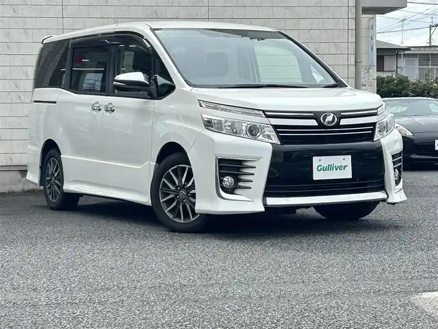トヨタ ヴォクシー ZS 煌 大分県 2015(平27)年 9.1万km ホワイトパールクリスタルシャイン ・社外メモリーナビ（MDV-Z701W）/　CD/DVD/BT/フルセグ/・ETC/・両側パワースライドドア/・社外フリップダウンモニター/・革巻きステアリング/・スマートキー/・エンジンプッシュスタート/・ウインカーミラー/・ステアリングスイッチ/・フロアマット/・ドアバイザー/・プライバシーガラス/・アイドリングストップ/・横滑り防止システム/・後部座席サンシェード/・純正16インチアルミホイール/・LEDヘッドライト/・純正フォグランプ/・保証書/・取扱説明書