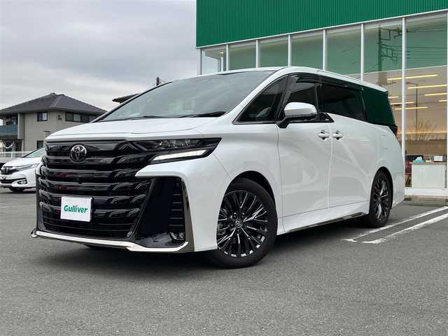 トヨタ ヴェルファイア ハイブリット Z プレミア 静岡県 2024(令6)年 0.6万km プラチナホワイトパールマイカ セキュリティーArgus/デジタルインナーミラー/エンジンスタートボタン/スマートキー（スペアキー１本）/パワーウィンドウ/パワーステアリング/MTモード付AT/100V充電/Wオートエアコン/クルーズコントロール/ETC2.0/USB入力端子/全方位カメラ/純正メーカーナビ（BT.フルセグ）/３列シート/ガラスルーフ/オットマン/電動リアゲート/ドライブレコーダー前後/ウォークスルー/フロアマット/D席N席パワーシート/D席N席セカンドシートシートヒーター/D席N席セカンドシートエアシート/両側パワースライドドア/純正アルミホイール/ABS/横滑り防止装置/コーナーセンサー前後/レーンキープアシスト/盗難防止装置/オートライト/オートマチックハイビーム/LEDライト/W+サイドエアバック/衝突軽減システム/ステアリングヒーター