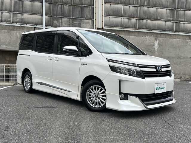 トヨタ ヴォクシー ハイブリッド V 愛知県 2015(平27)年 14.5万km ホワイトパールクリスタルシャイン ワンオーナー/置くだけ充電/モデリスタエアロ/革調シートカバー/純正SDナビ/フルセグTV・CD・DVD・SD・Bluetooth/バックカメラ/純正フリップダウンモニター/両側パワースライドドア/前席シートヒーター/LEDヘッドランプ/フォグランプ/ステアリングスイッチ/スマートキー/プッシュスタート/純正フロアマット/保証書/取扱説明書/スペアスマートキー