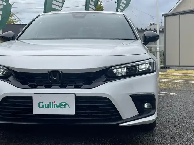 ホンダ シビック e:HEV 宮城県 2024(令6)年 1.5万km プラチナホワイトパール 純正リアスポイラー/純正ディスプレイオーディオナビ/フルセグＴＶ/BT/USB/AM/FM/スマートフォン連携/ホンダセンシング/・衝突軽減ブレーキ（CMBS）/・踏み間違い衝突軽減システム/・路外逸脱抑制機能/・歩行者事故低減ステアリング/・先行車発信お知らせ機能/・標識認識機能/・アダプティブドライビングビーム/・ブラインドスポットインフォメーション/・後退出庫サポート/・パーキングセンサーシステム/・ドライバー注意力モニター/・車線維持支援システム（LKAS）/ハーフレザーシート/D/N席パワーシート/シートヒーター/ワイヤレス充電/純正ドライブレコーダー（前後）/ビルトインＥＴＣ2.0/パドルシフト/電動パーキングブレーキ/オートブレーキホールド/カーテンエアバッグ/プッシュスタート/スマートキー×2/保証書/取扱説明書
