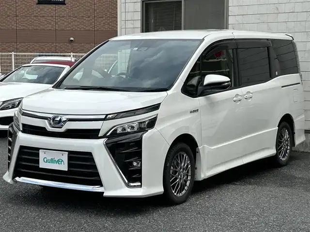 トヨタ ヴォクシー ハイブリッド ZS 福岡県 2017(平29)年 9.3万km ホワイトパールクリスタルシャイン ワンオーナー/エアロ（サイド）/純正10インチメモリナビ【NSZN-Z66T】/　（AM/FM/HDMI/Bluetooth/フルセグTV）/バックカメラ/純正12インチフリップダウンモニター　リモコン付き【V12T-R66C】/トヨタセーフティーセンス/・プリクラッシュセーフティー/・レーントレーシングサポート/・レーンディパーチャーアラート/・クルーズコントロール/・オートマチックハイビーム/・車両接近通報装置/・横滑り防止装置/・先行者発進アラーム/両側パワースライドドア/純正16インチアルミホイール/シートヒーター/黒色レザー調シートカバー/ビルトインETC/オートライト/フロントフォグランプ/盗難防止装置/電格ミラー/ドアバイザー/プッシュスタート/純正フロアマット/ISOFIX/2.1A電源プラグ×2/スペアキー×1/保証書/取扱説明書/ナビ取扱説明書