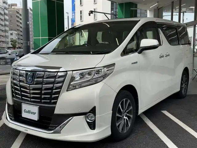トヨタ アルファードハイブリット G 広島県 2015(平27)年 7.8万km ラグジュアリーホワイトパールクリスタルシャインガラスフレーク ワンオーナー/純正メーカーオプション9.2インチSDナビ/・JBLサウンドシステム/・フルセグTV/・Bluetooth/パノラミックビューモニター/レーダークルーズコントロール/インテリジェントクリアランスソナー/プリクラッシュセーフティシステム/モデリスタエアロ/ツインムーンルーフ/両側パワースライドドア/パワーシート（D/N）/N席パワーオットマン/スマートキープッシュスタート