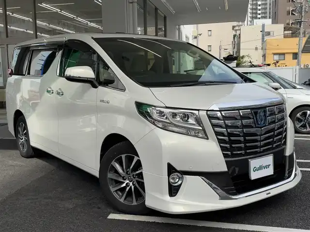 トヨタ アルファードハイブリット G 広島県 2015(平27)年 7.8万km ラグジュアリーホワイトパールクリスタルシャインガラスフレーク ワンオーナー/純正メーカーオプション9.2インチSDナビ/・JBLサウンドシステム/・フルセグTV/・Bluetooth/パノラミックビューモニター/レーダークルーズコントロール/インテリジェントクリアランスソナー/プリクラッシュセーフティシステム/モデリスタエアロ/ツインムーンルーフ/両側パワースライドドア/パワーシート（D/N）/N席パワーオットマン/スマートキープッシュスタート