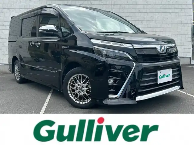 トヨタ ヴォクシー ハイブリッド ZS 煌 福岡県 2018(平30)年 7.7万km ブラック 社外９型ナビ/（AM/FM/CD/DVD/BT)/フルセグTV/バックカメラ/両側パワースライドドア /純正フリップダウンモニター/クルーズコントロール/ビルトインETC/スマートキー/プッシュスタート/前席シートヒーター /プリクラッシュ セーフティ/レーンキープアシスト/横滑り防止装置/純正１６インチAW/LEDヘッドライト/フロアマット/取り扱い説明書/保証書